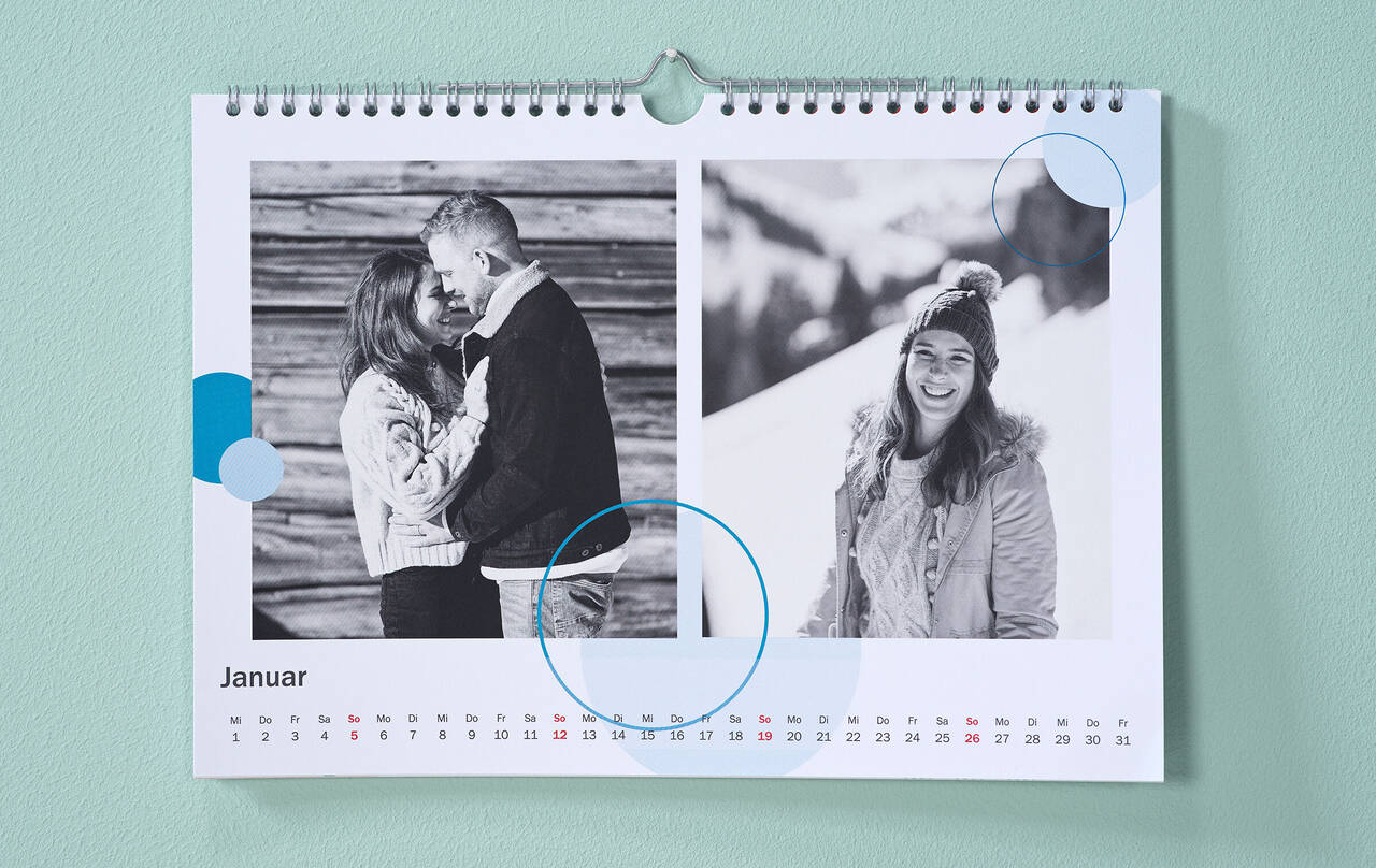 Kalender mit winterlichen Schwarz-Weiß-Fotos und kreisförmigen Cliparts in Blau hängt an einer mintgrünen Wand.