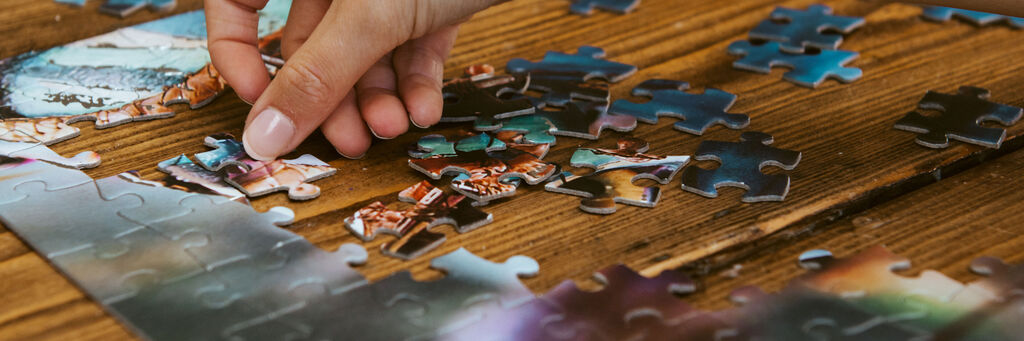 Eine Hand mit blau lackierten Nägeln fügt ein Puzzleteil ein, das auf einem Tisch liegt.