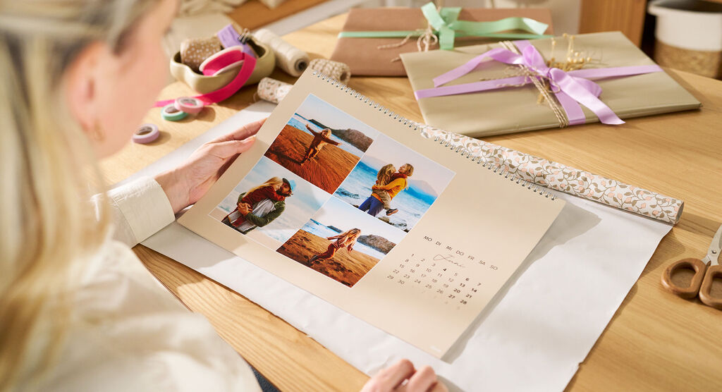 Eine Frau sitzt an einem Tisch und hält einen Wandkalender in den Händen, auf dem eine Fotocollage zu sehen ist.