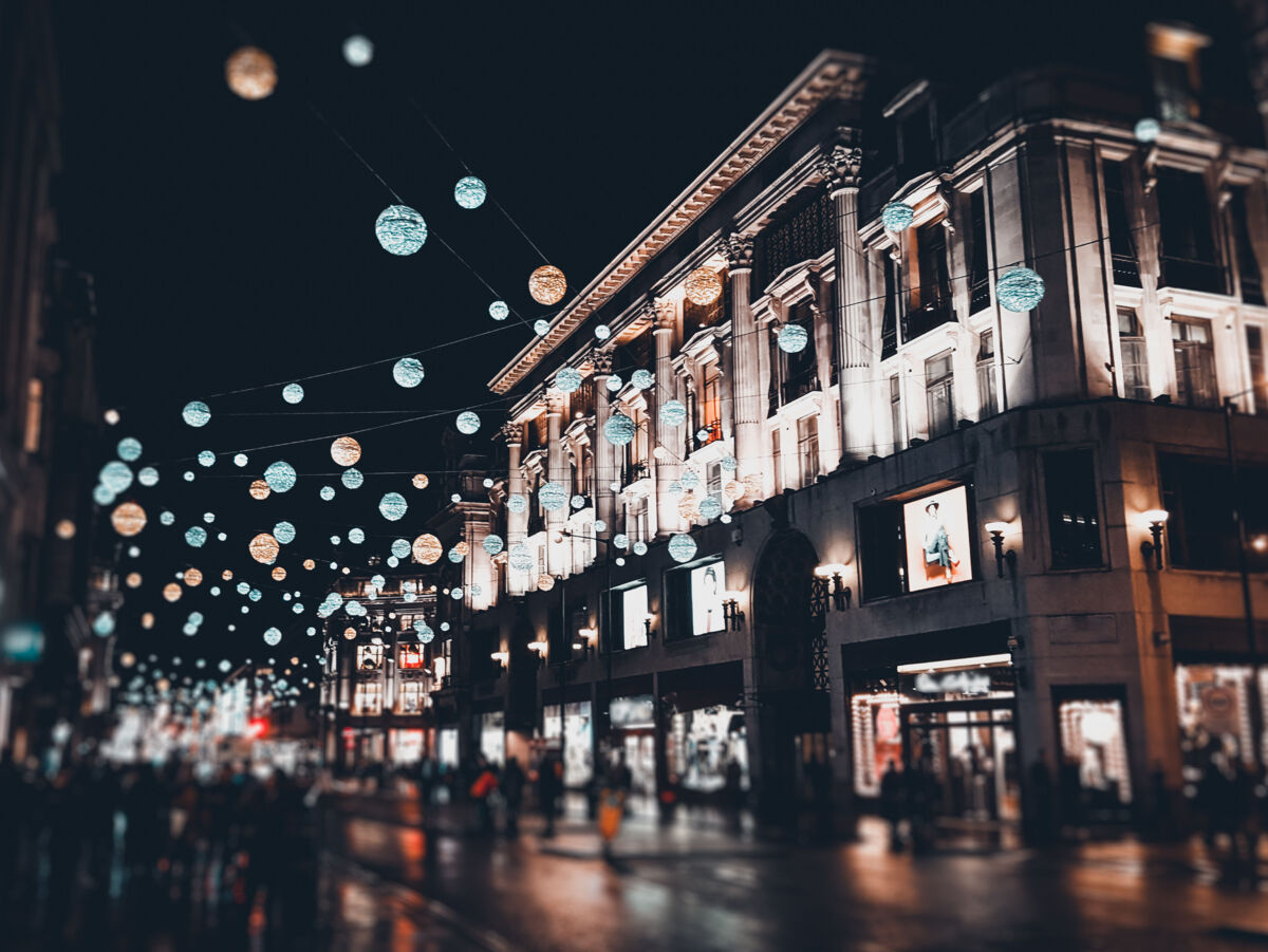 Regennasse Einkaufsstraße bei Nacht. Die Umgebung wird durch Weihnachtsbeleuchtung und Schaufenster beleuchtet.