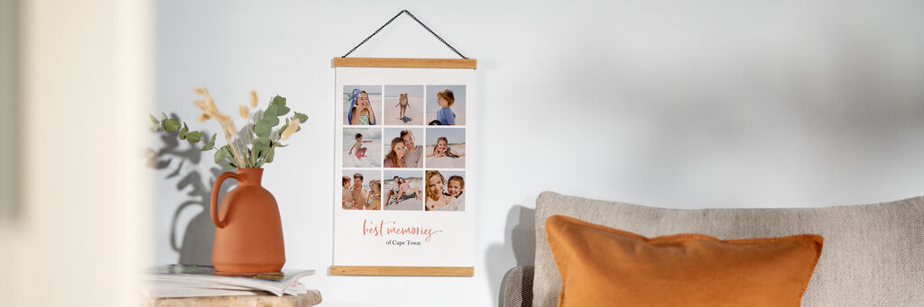 An einer Wand im Wohnzimmer hängt ein Poster mit Posterleiste. Darauf sind verschiedene kleine Fotos zu sehen, die Momente aus einem Familienurlaub zeigen.