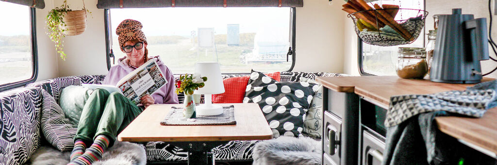Eine Frau sitzt in der gemütlichen, modernen Sitzecke eines Wohnwagens und hält ein aufgeschlagenes Fotobuch und den Händen.
