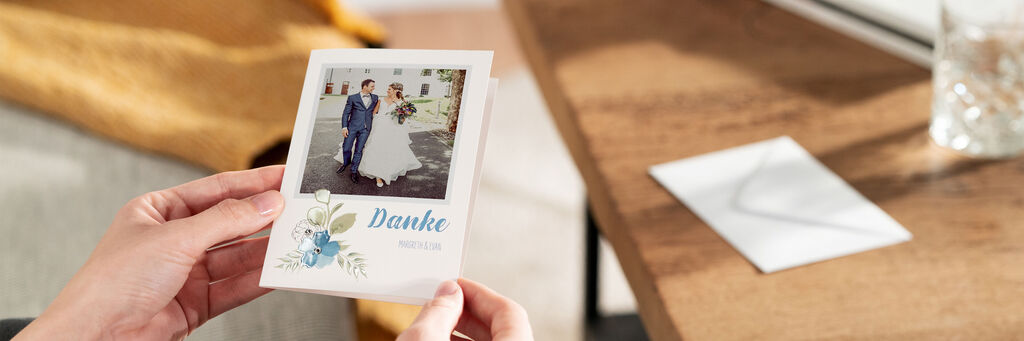 Zwei Hände halten eine Klappkarte. Darauf ist ein Foto eines Brautpaares zu erkennen. Darunter steht das Wort „Danke“.
