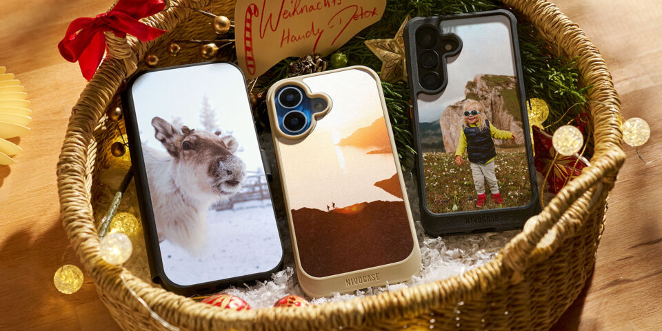 Personalisierte Handyhüllen in einem Geschenkkorb, umgeben von Weihnachtsdekoration.