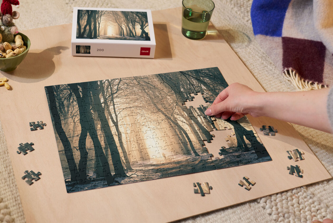 Fotopuzzle wird auf einer Holzplatte, die auf einem Teppich liegt, von einer Person gepuzzelt.