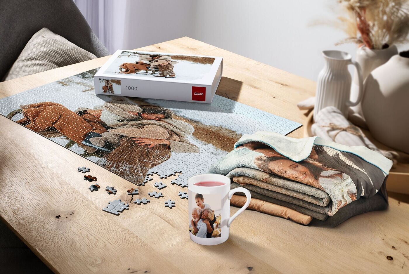 Ein liebevoll gestaltetes Puzzle liegt auf einem Tisch. Daneben ist eine Tasse mit einem Familienfoto und eine Decke mit weiteren Bildern zu sehen. Die Atmosphäre ist einladend und warm.