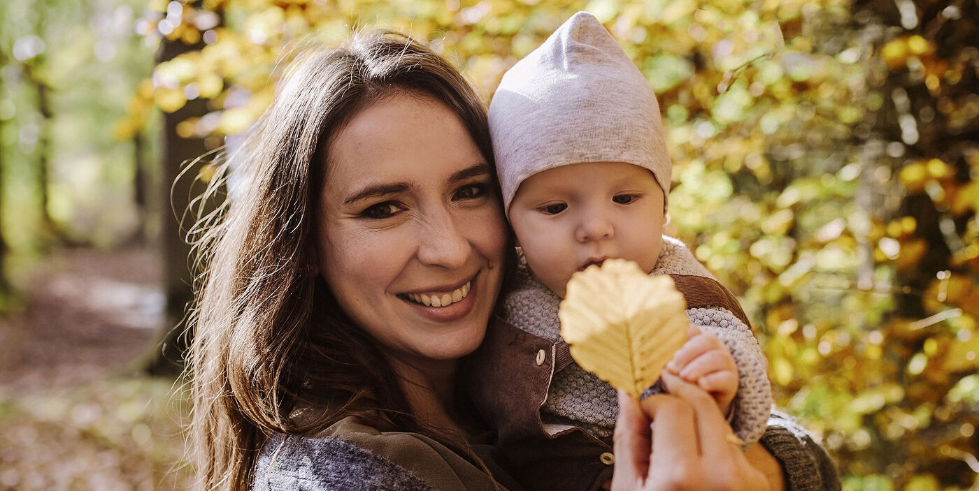 Person und Baby genießen einen sonnigen Herbsttag im bunten Wald mit gelbem Blatt