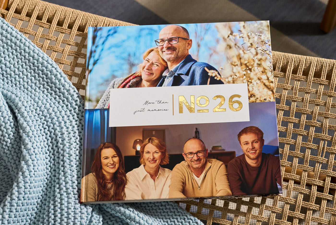 CEWE FOTOBUCH „N°26“ mit Fotos eines Paares und einer Familie von vier Personen auf einem geflochtenen Stuhl mit blauer Decke.