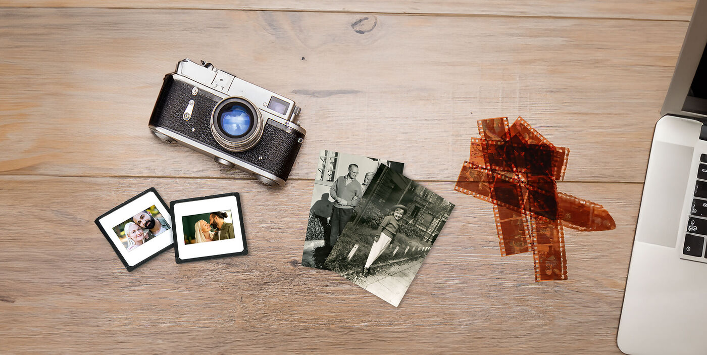 Kamera, Dias, Schwarzweißfotos und Filmnegative liegen zusammen mit einem Laptop auf einem Holztisch