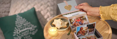 Eine Hand öffnet ein Falt-Buch mit Fotos und zieht den Streifen aus einer Box au einem weihnachtlich dekorierten Tisch.