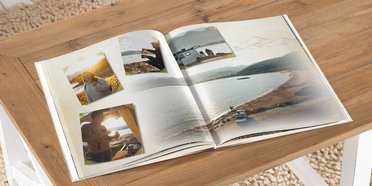 Es ist eine Doppelseite aus einem CEWE FOTOBUCH von Annika und Mathias Koch zu sehen. Das Buch liegt auf einem Tisch. Es zeigt eine Landschaftsaufnahme eines Strandes im Hintergrund und einige Impressioenen als Collage über das Bild verteilt.