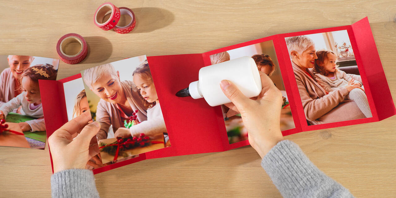 Zwei Hände kleben Fotos von einem Kind mit Großmutter auf einen roten Hintergrund.