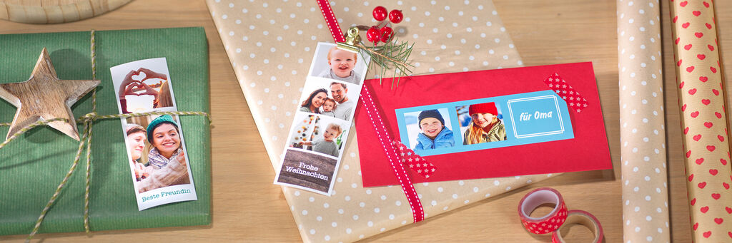 Zwei festlich verpackte Geschenke mit Sofortfoto-Anhängern liegen auf einer Tischplatte neben weihnachtlicher Deko mit Kerze und Geschenkpapier.