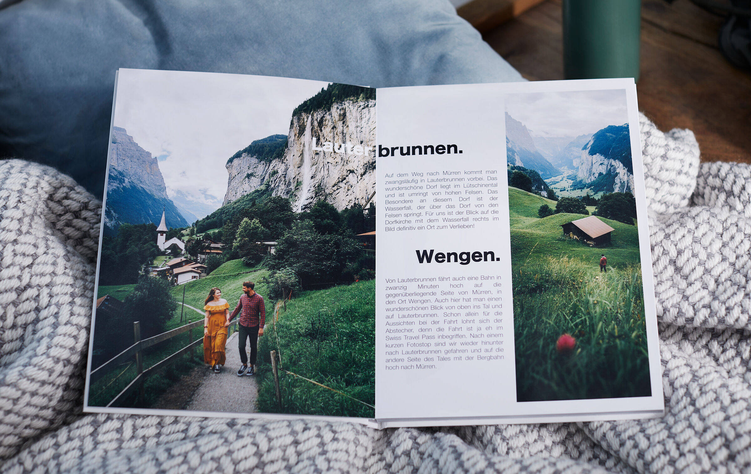 Auf einer Decke liegt das aufgeklappte CEWE FOTOBUCH Schweiz mit einer gestalteten Doppelseite.