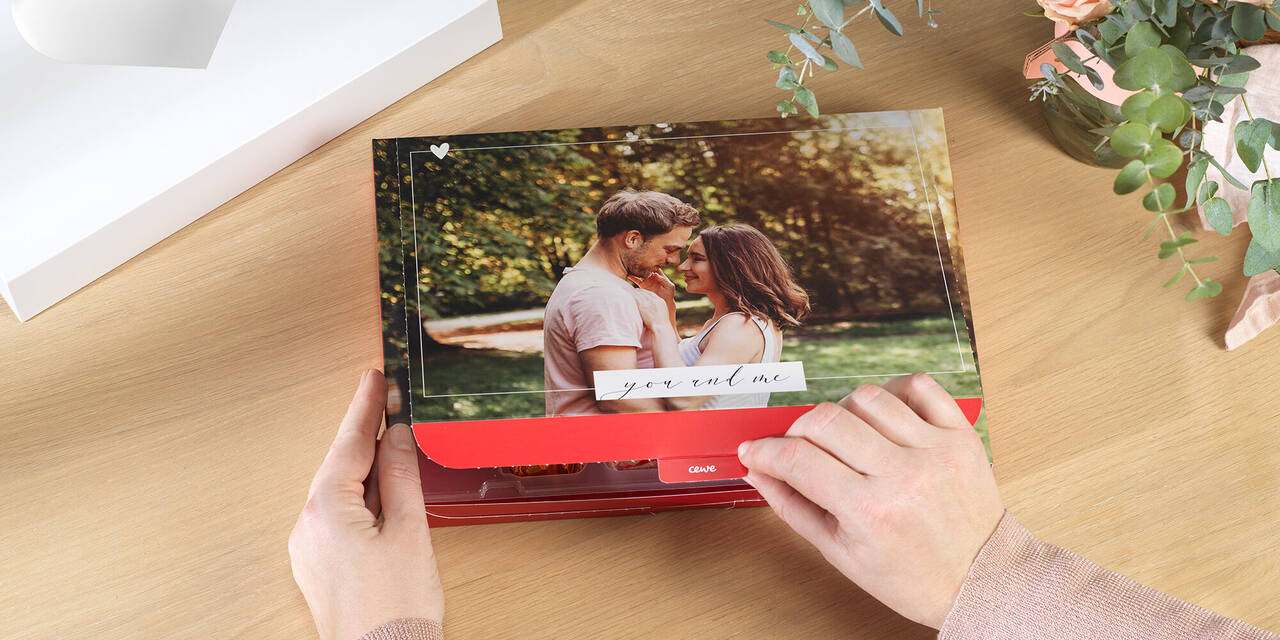 Hand öffnet Foto-Geschenkbox. Auf dem Deckel ist das Foto eines Pärchens zu sehen. Das Bild wird von einem Design umrandet, auf dem „you and me“ steht.