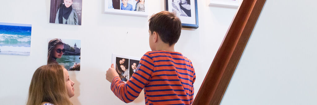 Die Kinder von Anna hängen im Treppenhaus gemeinsam Bilder auf.