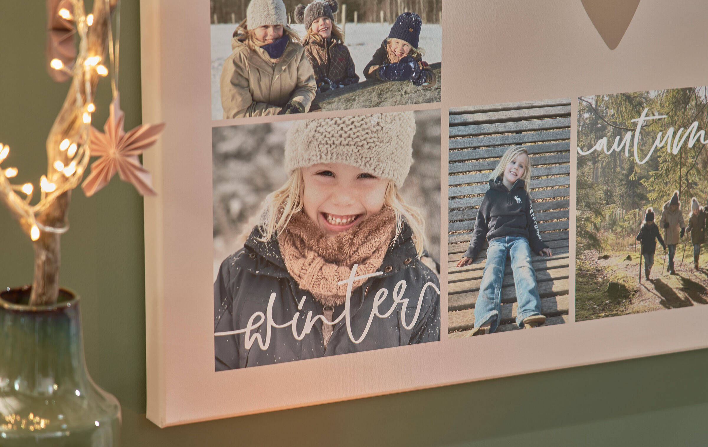 Nahaufnahme einer Fotoleinwand, auf der verschiedene Fotos einer Familie zu sehen sind. Darauf stehen außerdem die Worte „Winter“ und „Autumn“. Links neben der Leinwand ist weihnachtliche Dekoration erkennbar.