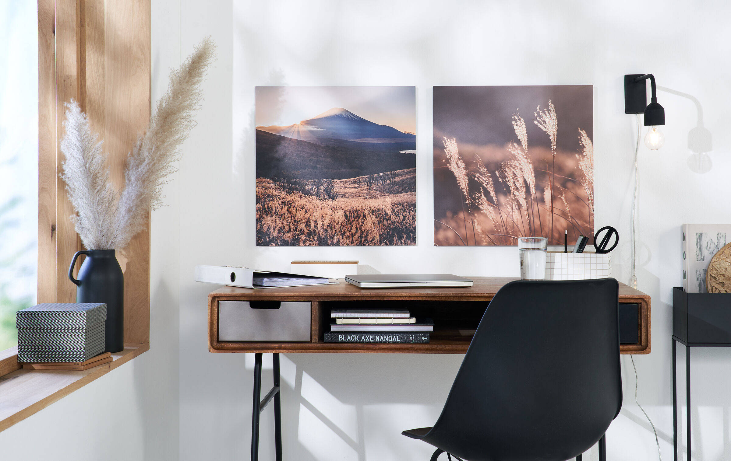 Über einem Schreibtisch hängen zwei Wandbilder. Links ist eine Landschaft zu sehen, rechts eine farblich passende Nahaufnahme von Pampasgras.
