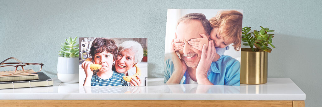 Zwei Art Prints mit Aufnahmen von Enkeln und Großeltern sind auf einem Sideboard mit weiteren Deko- Objekten arrangiert.