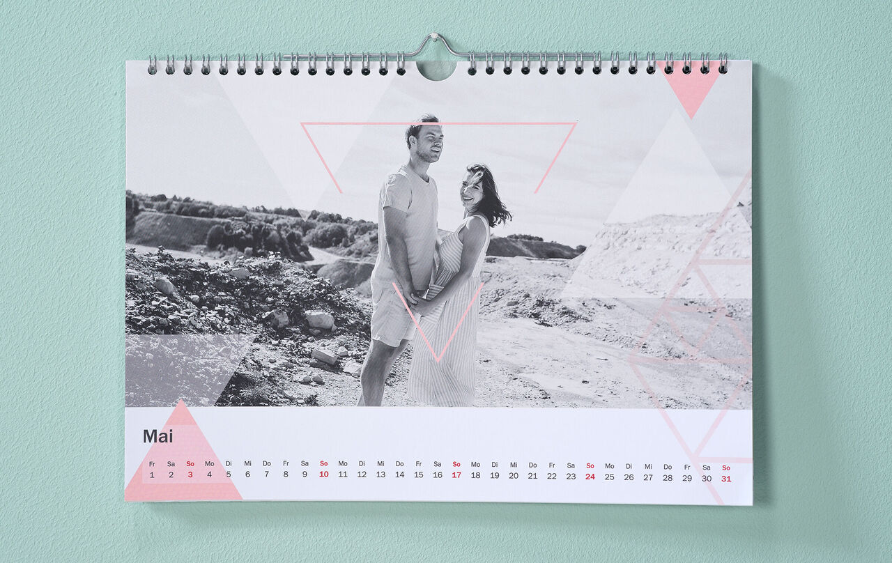 Kalender mit Pärchenfoto in Schwarz-Weiß und dreieckigen Cliparts in Pastell hängt an mintgrüner Wand.