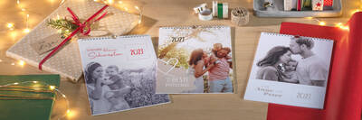 Drei Kalender liegen neben weihnachtlicher Dekoration wie Geschenkpapier und Lichterkette auf einem Tisch.